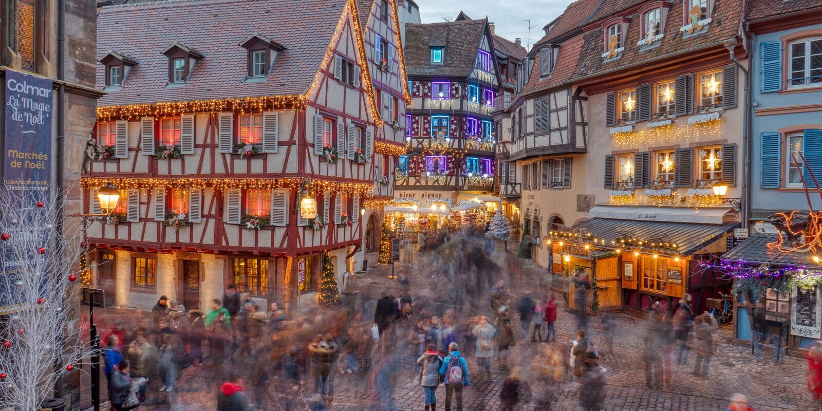 Half-timbered houses decorated with Christmas lights above a busy square in Colmar