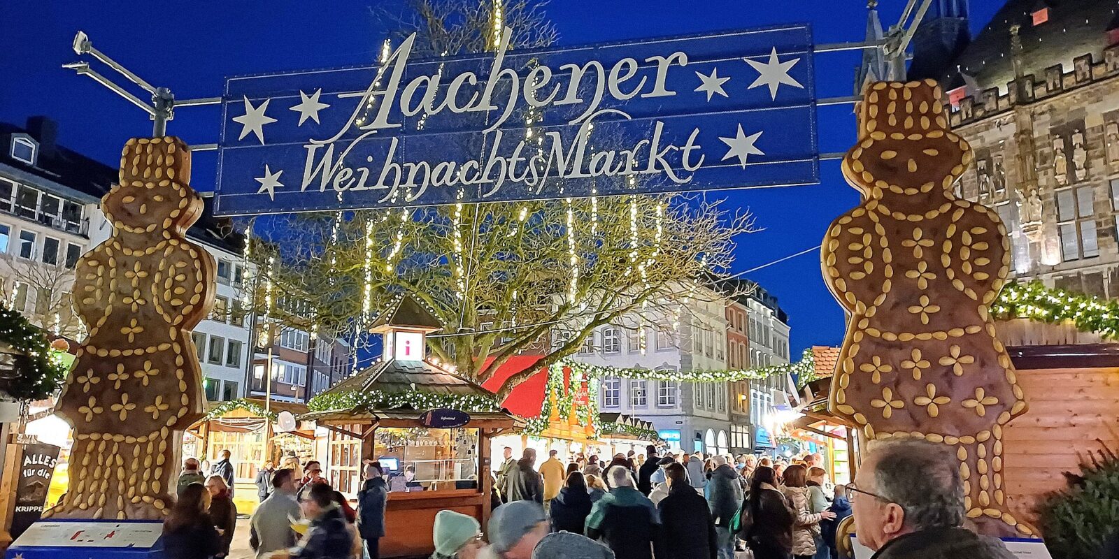 The illuminated Aachener Weihnachtsmarkt entrance arch flanked by giant Printen gingerbread figures
