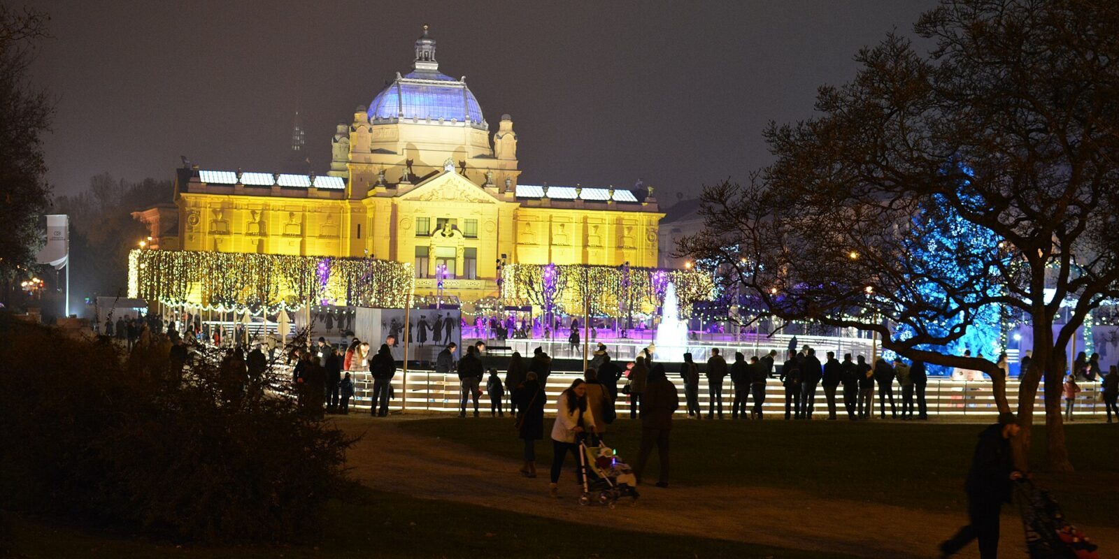 The Art Pavilion in Zagreb lit up at night during Advent, with crowds in the park in front